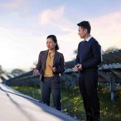 Woman and man standing outside at solar farm, discussing solar panels at sunset.