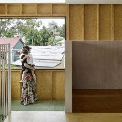 Woman holding small child in house looking out window opening