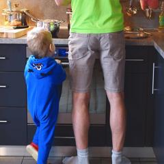 photo of child standing next to adult in kitchen