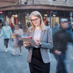 business woman in busy street looking at tablet
