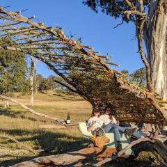 UQ architecture students Siubhan Rudge (L) and Lara Rann (R) sitting under the pavilion they'd constructed by hand using available materials